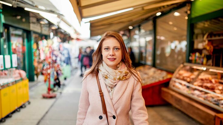 Eine junge lächelnde Frau macht Einkäufe am Wiener Naschmarkt.