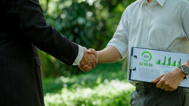 Fokus auf zwei Männer, die Hände schütteln, einer mit ESG-Report unter dem Arm