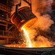 ein riesiger Kessel, aus dem leuchtendes geschmolzenes Metall fließt, in einer dunklen, doch lebhaften industriellen Umgebung