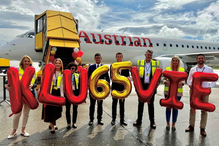 Mitarbeitende vom Flughafen Klagenfurt und den Austrian Airlines halten auf Rollfeld mit Flugzeug im Hintergrund bunte Ballone hoch