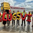 Mitarbeitende vom Flughafen Klagenfurt und den Austrian Airlines halten auf Rollfeld mit Flugzeug im Hintergrund bunte Ballone hoch
