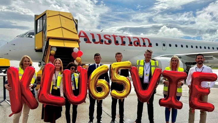 Mitarbeitende vom Flughafen Klagenfurt und den Austrian Airlines halten auf Rollfeld mit Flugzeug im Hintergrund bunte Ballone hoch