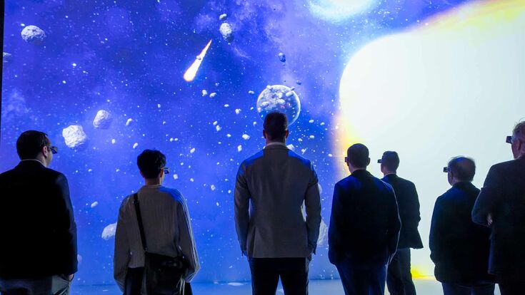 Mehrere Menschen blicken beim DNA Summit 2025 bei Wacker Neuson mit VR-Brillen auf eine große Leinwand mit Meteoriten.
