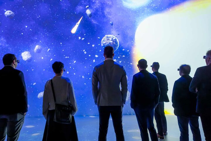 Mehrere Menschen blicken beim DNA Summit 2025 bei Wacker Neuson mit VR-Brillen auf eine große Leinwand mit Meteoriten.