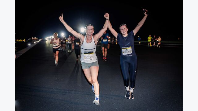 Zwei junge Läuferinnen beim Klagenfurt Airport Night Run 2024 laufen und jubeln gemeinsam.