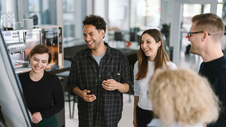 Mehrere junge Menschen stehen an der TU Graz um ein Whiteboard und lachen.