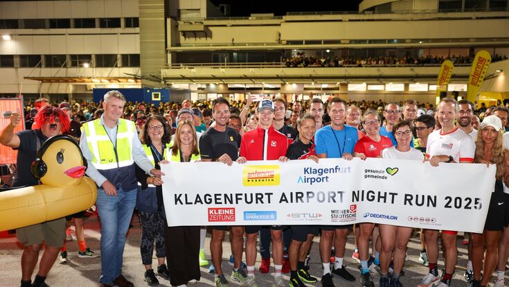 Viele Läuferinnen und Läufer halten beim Klagenfurt Airport Night Run 2025 ein Transparent hoch.