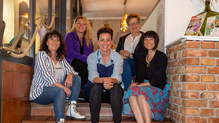Fünf Frauen in der Initiative G'lernt is g'lernt sitzen gemeinsam auf Stufen.