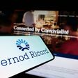 Pernod Ricard-Schriftzug auf einem Smartphone, im Hintergrund verschwommen eine Bar.