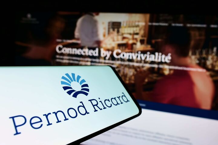 Pernod Ricard-Schriftzug auf einem Smartphone, im Hintergrund verschwommen eine Bar.
