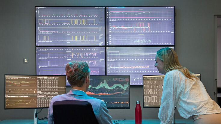 2 Personen vor mehreren Bildschirmen, Datenanalyse