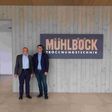 Unternehmensgründer Kurt Mühlböck und Richard Mühlböck, Geschäftsführer der Mühlböck Holztrocknungsanlagen GmbH stehen in neuem Firmensitz neben Firmenschild.