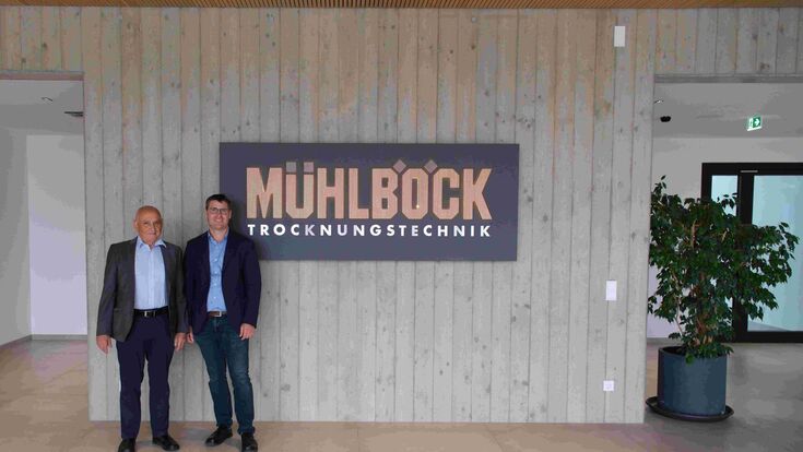 Unternehmensgründer Kurt Mühlböck und Richard Mühlböck, Geschäftsführer der Mühlböck Holztrocknungsanlagen GmbH stehen in neuem Firmensitz neben Firmenschild.