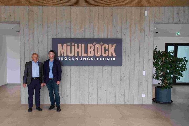 Unternehmensgründer Kurt Mühlböck und Richard Mühlböck, Geschäftsführer der Mühlböck Holztrocknungsanlagen GmbH stehen in neuem Firmensitz neben Firmenschild.