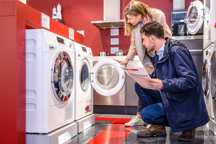 Eine junge Frau und ein junger Mann shoppen in einem kleinen Geschäft nach einer neuen Waschmaschine.