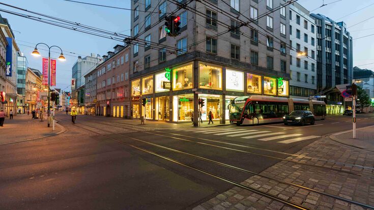 Landstraße Linz in Oberösterreich mit wenigen Menschen, einem Auto und einer Straßenbahn an einer Kreuzung in der Abenddämmerung.