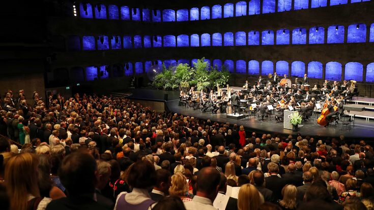 Publikum blickt bei Eröffnung der Salzburger Festspiele auf das schwarz gekleidete, spielende Orchester auf der Bühne