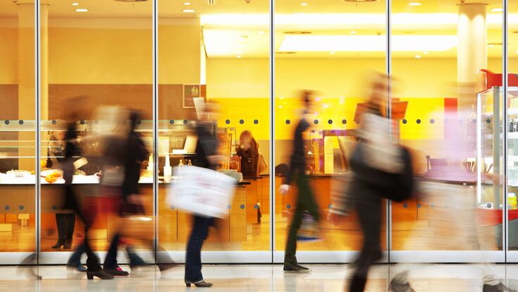 Verschwommene, schnell gehende Menschen mit Einkaufstaschen in einem Shopping Center.