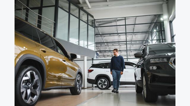 Ein junger Mann flaniert zwischen neuen SUVs bei einem großen Autohändler.