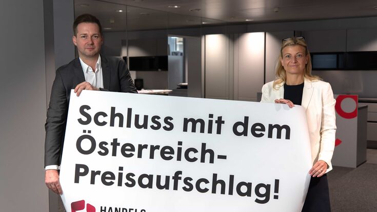 Rainer Will vom Handelsverband & Barbara Teiber von der GPA halten ein Transparent, das Ende von Österreich-Preisaufschlag fordert.