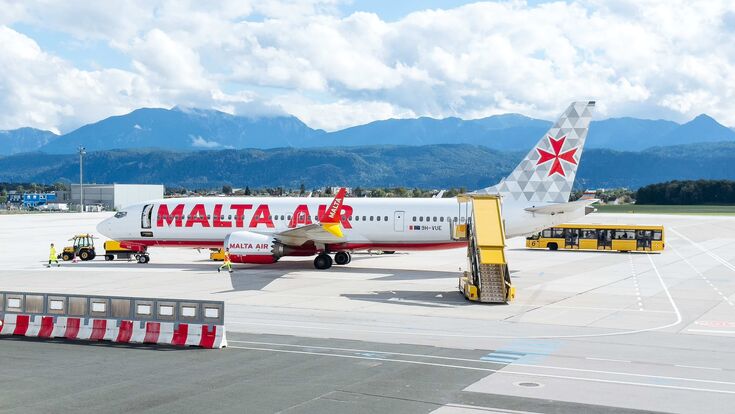 Eine Malta Air-Maschine steht am Flughafen Klagenfurt, Berge im Hintergrund.