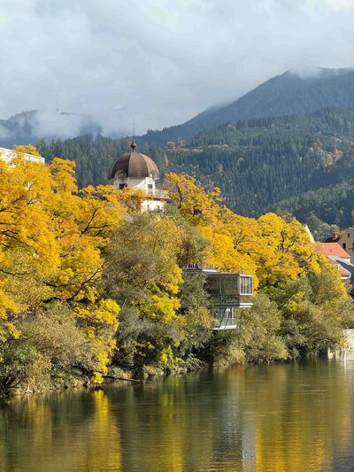 Der Schwammerlturm in Leoben, Steiermark, aus der Ferne, halb verdeckt von herbstlichen Bäumen.
