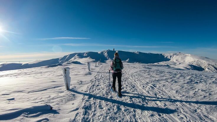 Rückenansicht auf Frau in Schneestiefeln am Gipfel der Lavanttaler Alpen in Steiermark bzw Kärnten bei Sonnenschein, der Grund schneebedeckt