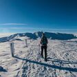 Rückenansicht auf Frau in Schneestiefeln am Gipfel der Lavanttaler Alpen in Steiermark bzw Kärnten bei Sonnenschein, der Grund schneebedeckt