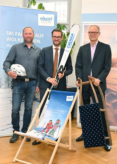 Markus Reiser, Obmann und Vorstand des Kärntner Skischulverbandes, Tourismuslandesrat Sebastian Schuschnig und Klaus Ehrenbrandtner, Geschäftsführer der Kärnten Werbung, präsentieren Kampagne für Kärntens Wintersaison 2025/26 mit Liegestuhl und Ski.