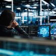 Rückenansicht auf einen Menschen in großem dunklen Raum mit vielen Computern, der Bildschirm vor ihm zeigt leuchtendes neuronales netzwerk