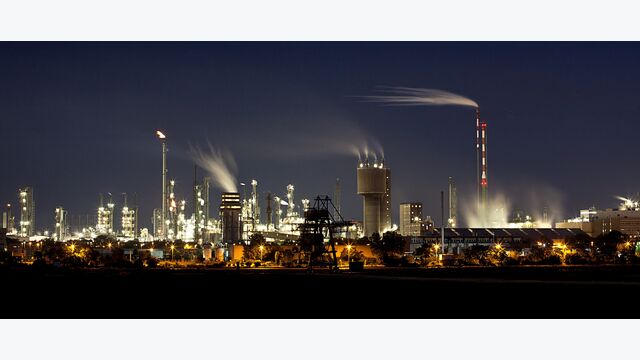 große erleuchtete fabrik bei nacht, wind weht rauch von schornsteinen weg