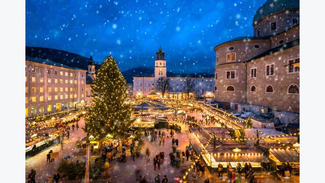 Christkindlmarkt am Abend mit Menschen und fallenden Schneeflocken auf dem Domplatz in Salzburg Stadt, Österreich