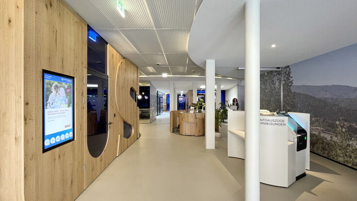 Volksbank Filiale in Österreich von innen, mit großem Empfangsbereich, Automaten und weit im Hintergrund eine Frau