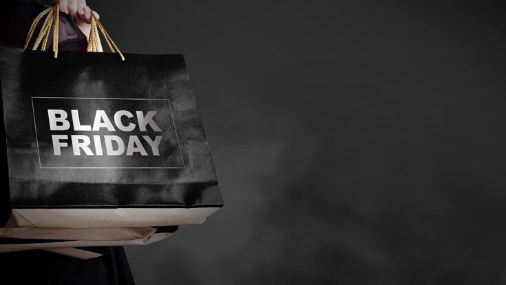 Eine Hand trägt schwarze Einkaufstaschen mit der Aufschrift Black Friday vor einem schwarzen Hintergrund mit einem Hauch von Rauch oder Nebel