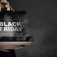 Eine Hand trägt schwarze Einkaufstaschen mit der Aufschrift Black Friday vor einem schwarzen Hintergrund mit einem Hauch von Rauch oder Nebel