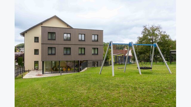 Außenansicht auf Gebäude des SchülerInnenwohnens in Schwertberg, Oberösterreich, der Sozialen Initiative, mit Rasen und Schaukel im Vordergrund