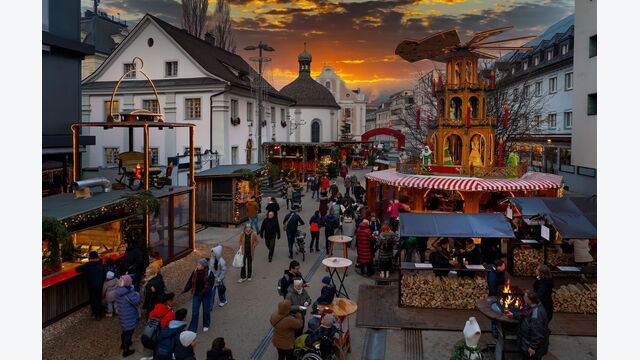 Adventmarkt/Weihnachtsmarkt in Bregenz, Vorarlberg, Österreich, mit einigen Besuchern an Ständen in Abenddämmerung