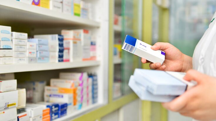 Nahaufnahme auf Hände einer Apothekerin, die Medikamten in ein Regal einschlichtet.