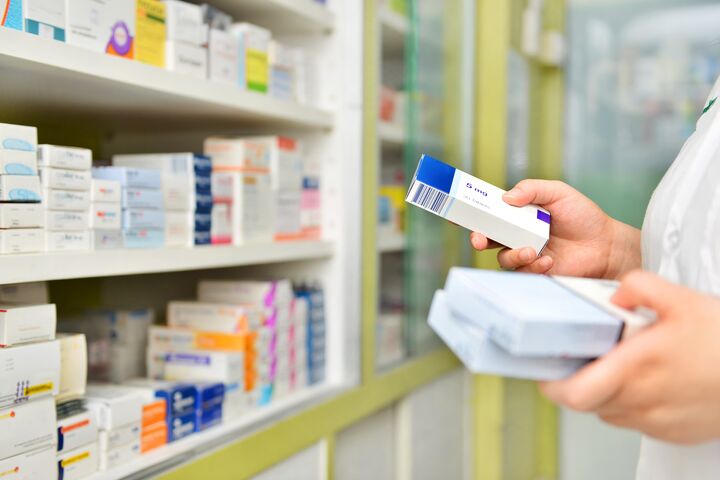 Nahaufnahme auf Hände einer Apothekerin, die Medikamten in ein Regal einschlichtet.
