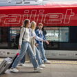 drei fröhliche Jugendliche ziehen kleine koffer am Bahnsteig vor einem öbb Railjet