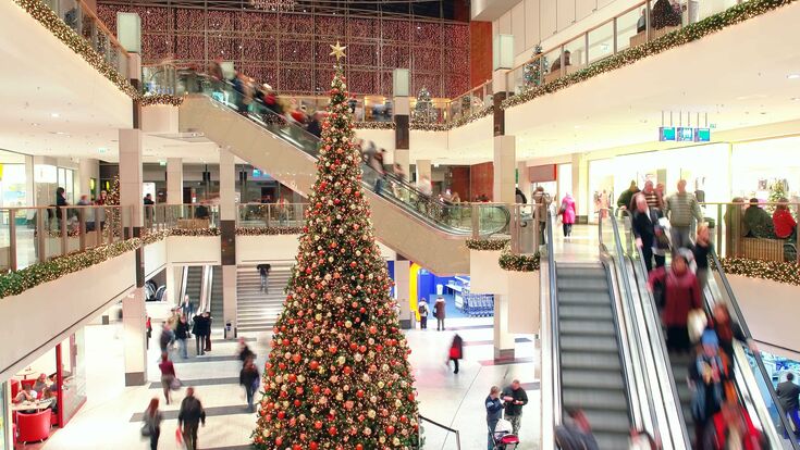ein mehrstöckiges einkaufszentrum mit besuchern auf rolltreppen, in der mitte ein riesiger weihnachtsbaum