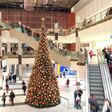 ein mehrstöckiges einkaufszentrum mit besuchern auf rolltreppen, in der mitte ein riesiger weihnachtsbaum