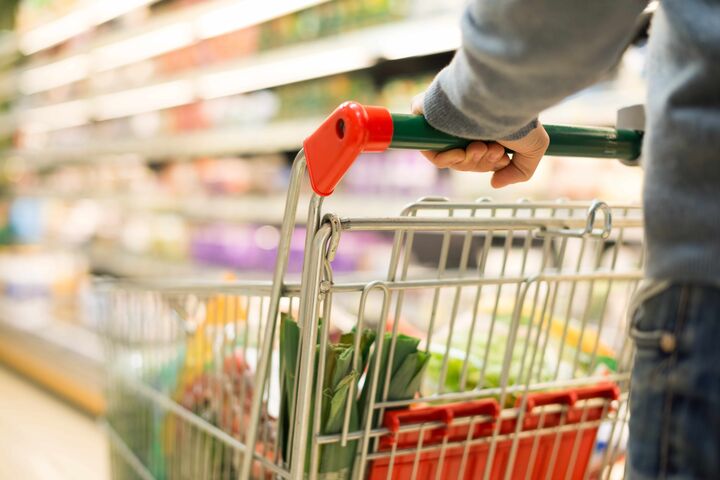 detailansicht auf hände, die einen einkaufswagen mit lebensmitteln durch einen supermarkt schieben