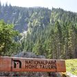 Holzschild mit Aufschrift "Nationalpark Hohe Tauern" mit Wiese und Wald im Hintergrund