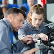 junge frau (weiblicher lehrling) wird von einem mann in der automechanik angeleitet