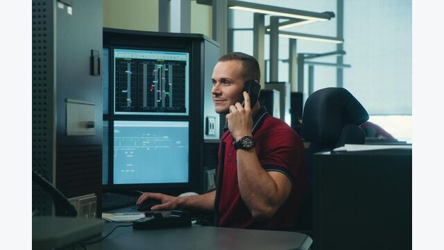 junger fahrdienstleiter der öbb sitzt am telefon vor computer