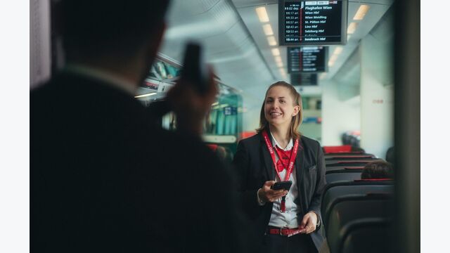 junge zugbegleiterin bei den öbb lächelt einen fahrgast an