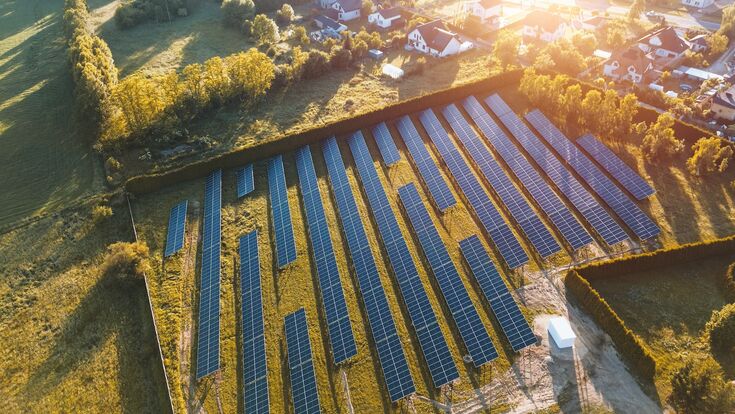 Luftansicht auf mehrere große solarpanele im grünen neben kleiner ortschaft