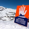 ein oranges schild vor einem verschneiten berg zeigt eine warnende hand und warnt vor lawinengefahr