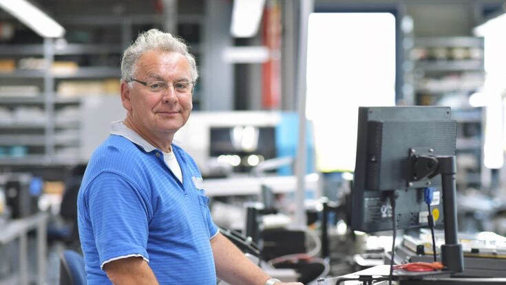 alter mann arbeitet stehend an einem computer in einer industrieanlage